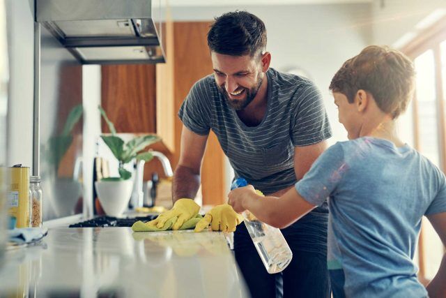 An adult and child grin while cleaning the kitchen with Warsaw Chemical.