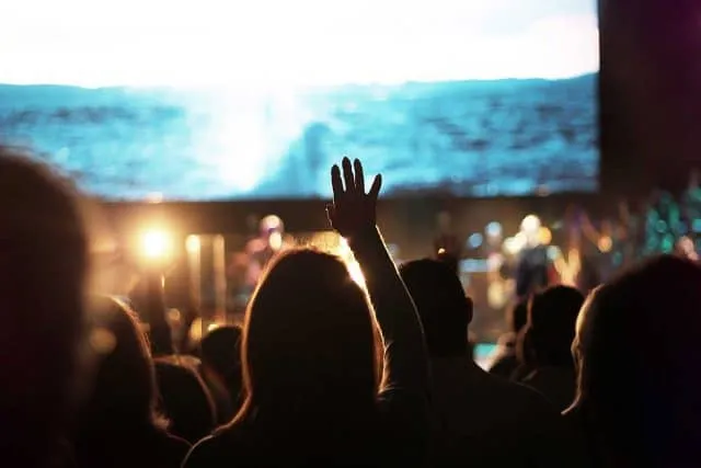 Audience with raised hand at a concert, bright stage lights in the background.