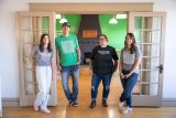 Four people standing in a green-walled room, ready to be great online.