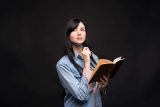Woman in denim shirt with notebook, pondering how to write a press release.