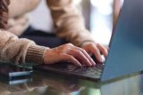 Person typing on a laptop at a glass table, doing a social media profile audit.