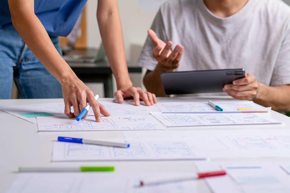 Two people review high-converting homepage design sketches spread on a table.