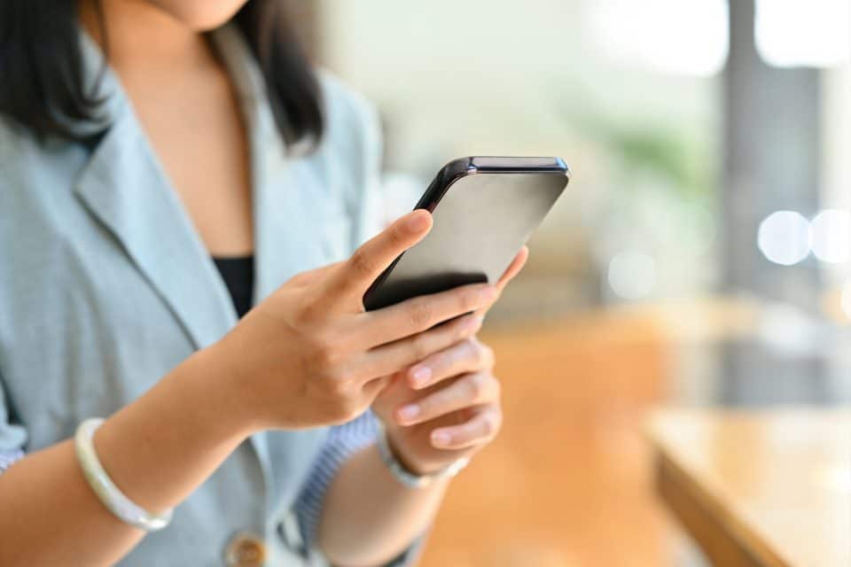 Person using a smartphone indoors, wearing a light jacket, texts for SMS marketing.