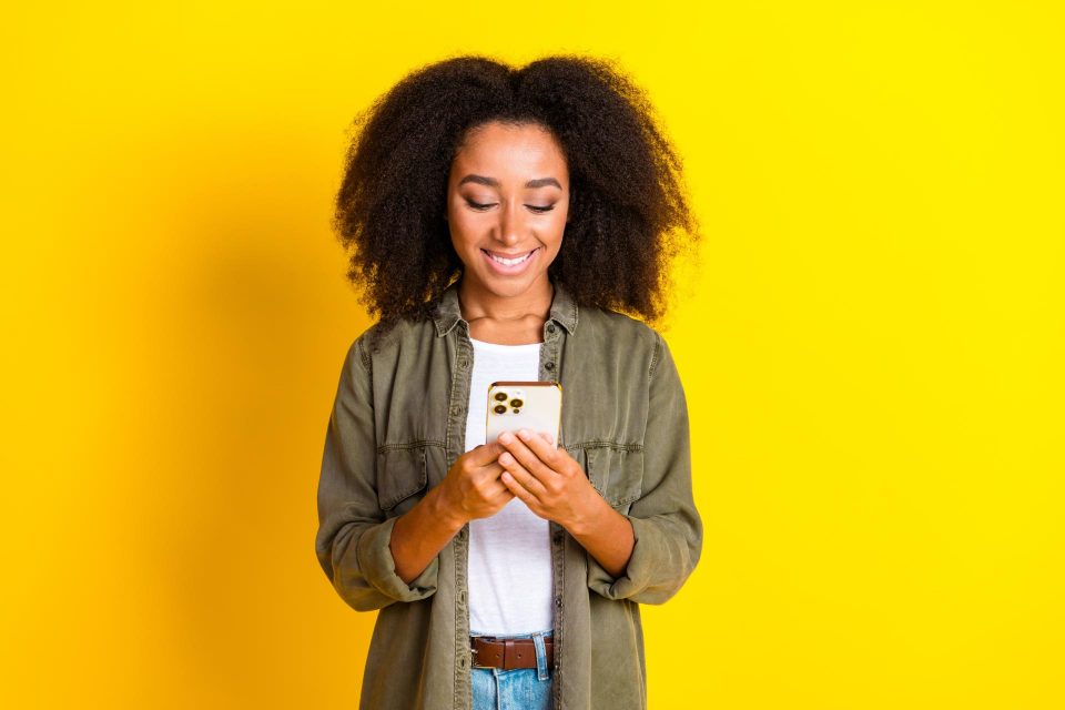 Woman smiling while enjoying online content writing on her smartphone.