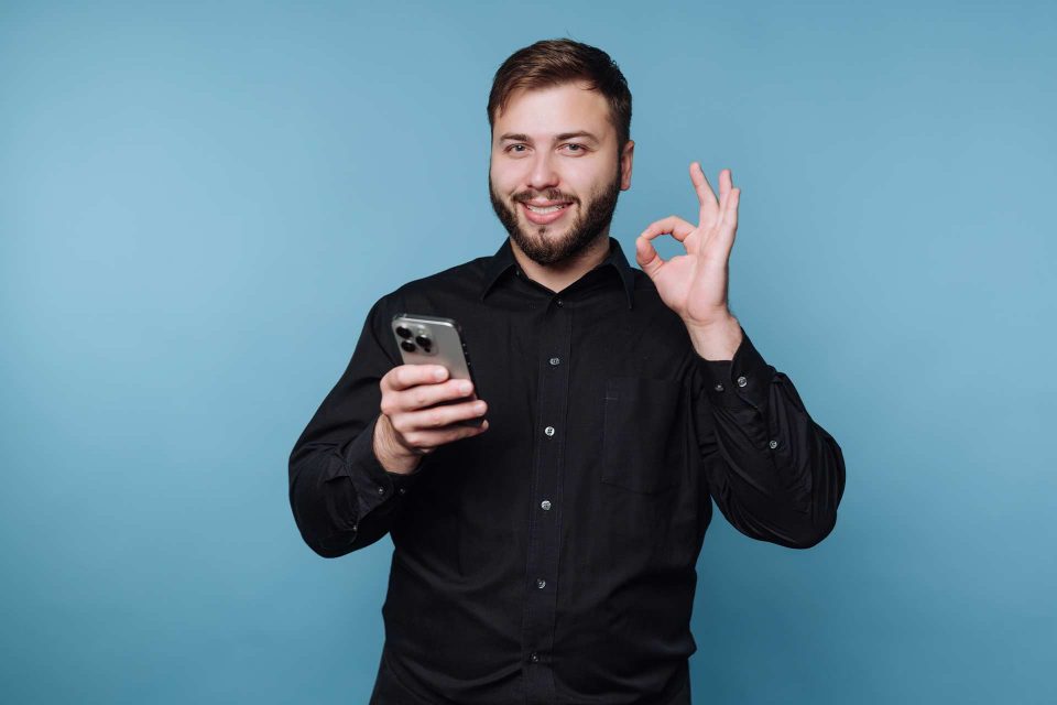 Man in black shirt holding smartphone, gesturing OK—perfect for email subject lines.