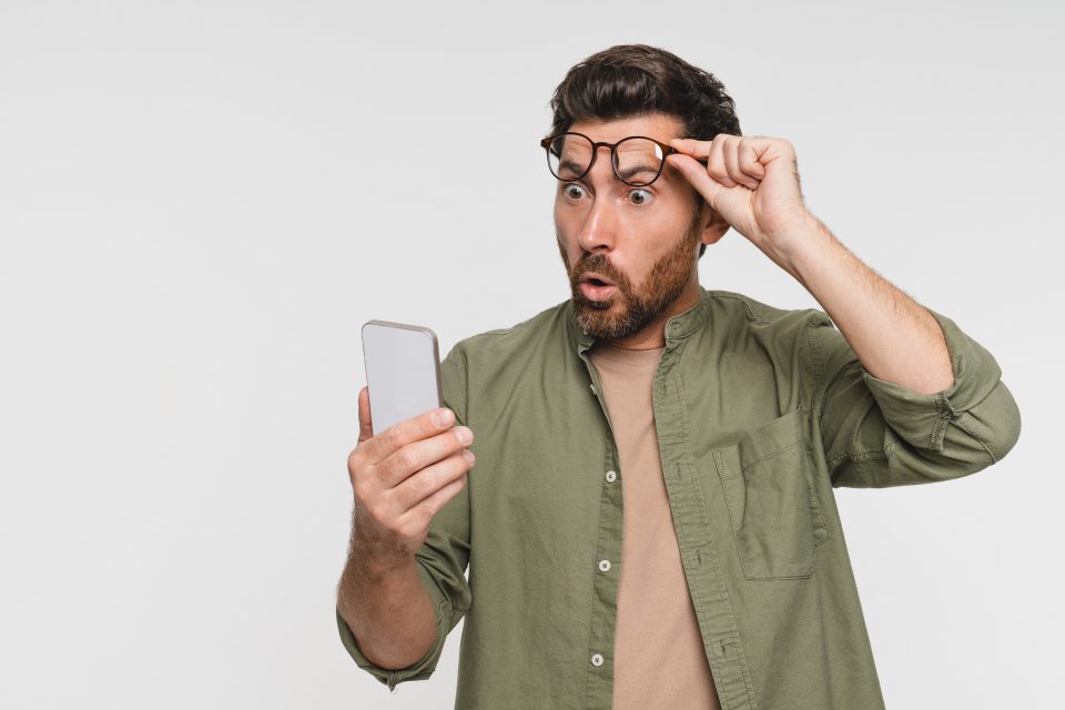 Man lifting glasses, surprised by digital marketing account setup on smartphone.