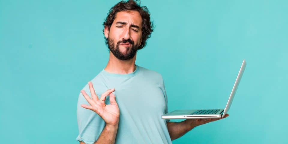 Man in a light blue shirt holding a laptop, making an OK gesture for digital marketing.