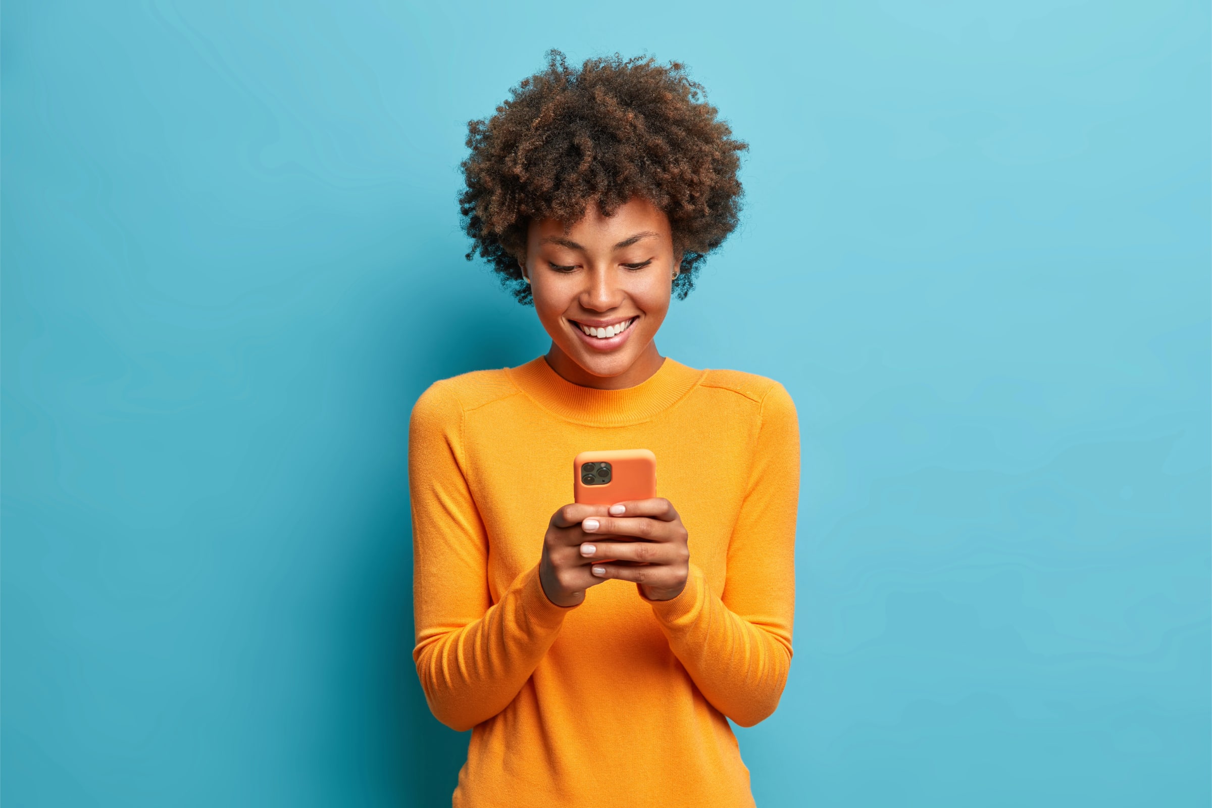 Smiling person in orange sweater using smartphone for digital marketing keywords.