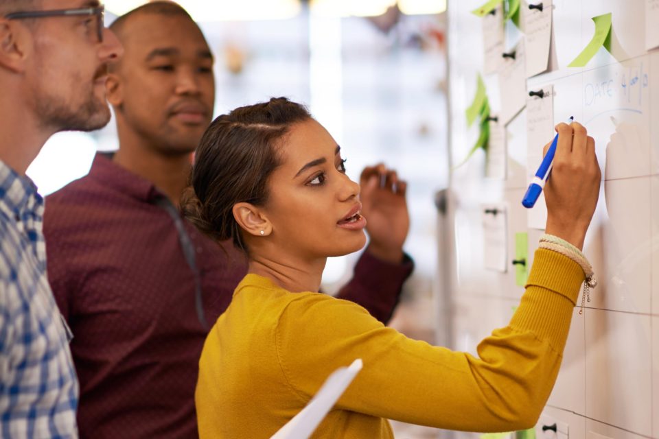 Woman illustrates storytelling in marketing on a whiteboard as colleagues observe.