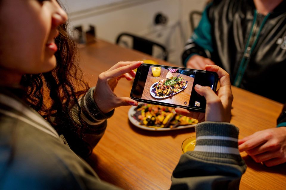 Person snapping food pics at a wooden table—social media photography tips in action.