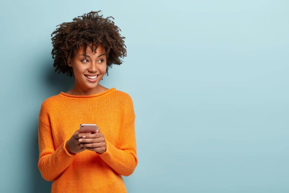 Person in orange sweater holds a smartphone, standing against a blue background.