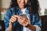 A woman smiles while using a smartphone for a marketing audit.