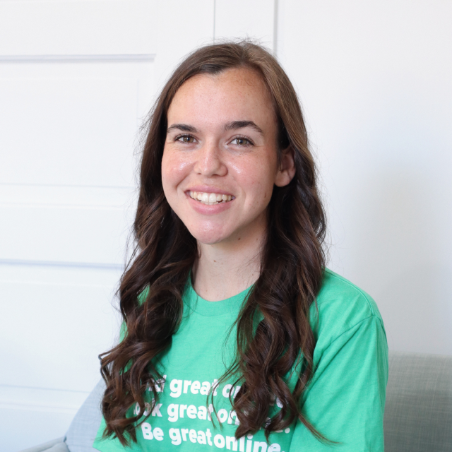 Young woman with long brown hair smiling, wearing a green T-shirt, indoors.