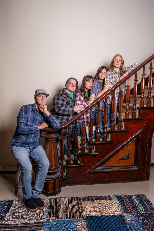 Five people in plaid shirts pose by a wooden staircase—meet the team.