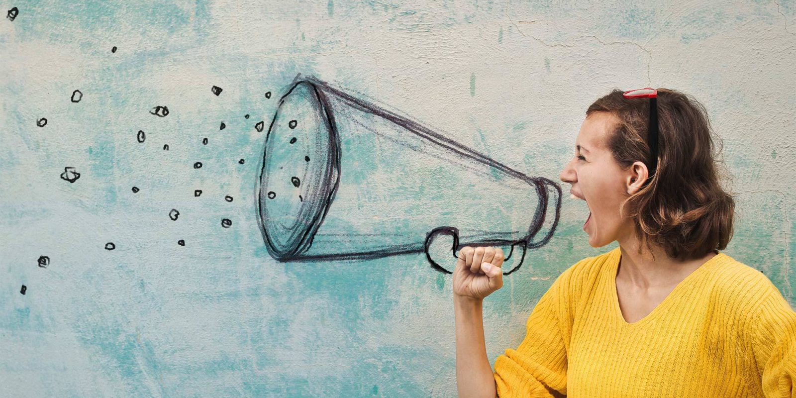 caucasian brunette woman in a yellow sweater yelling into a pretend megaphone about digital marketing services