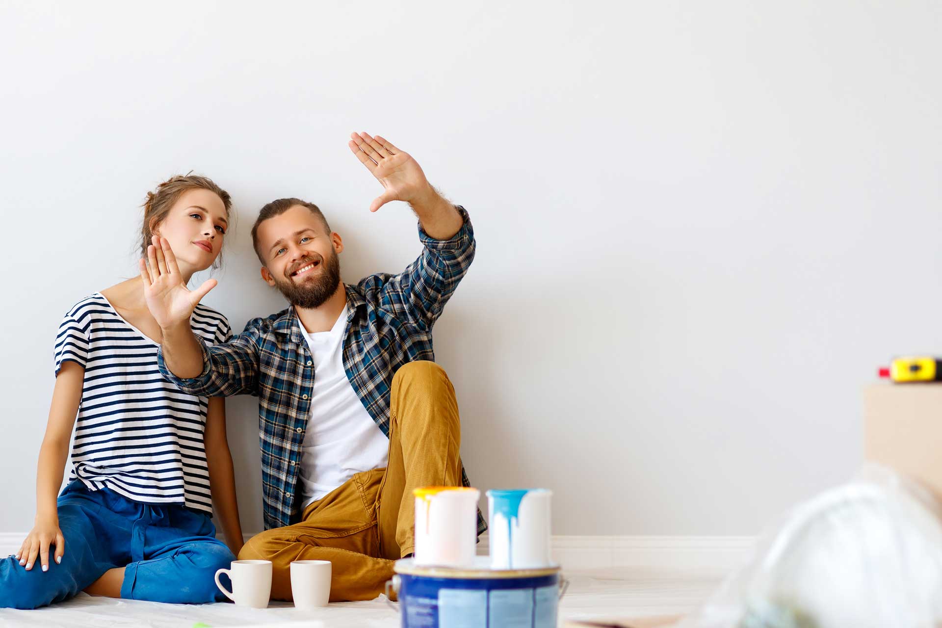 Two people sitting on floor, holding paint sample, with cans and mugs nearby.