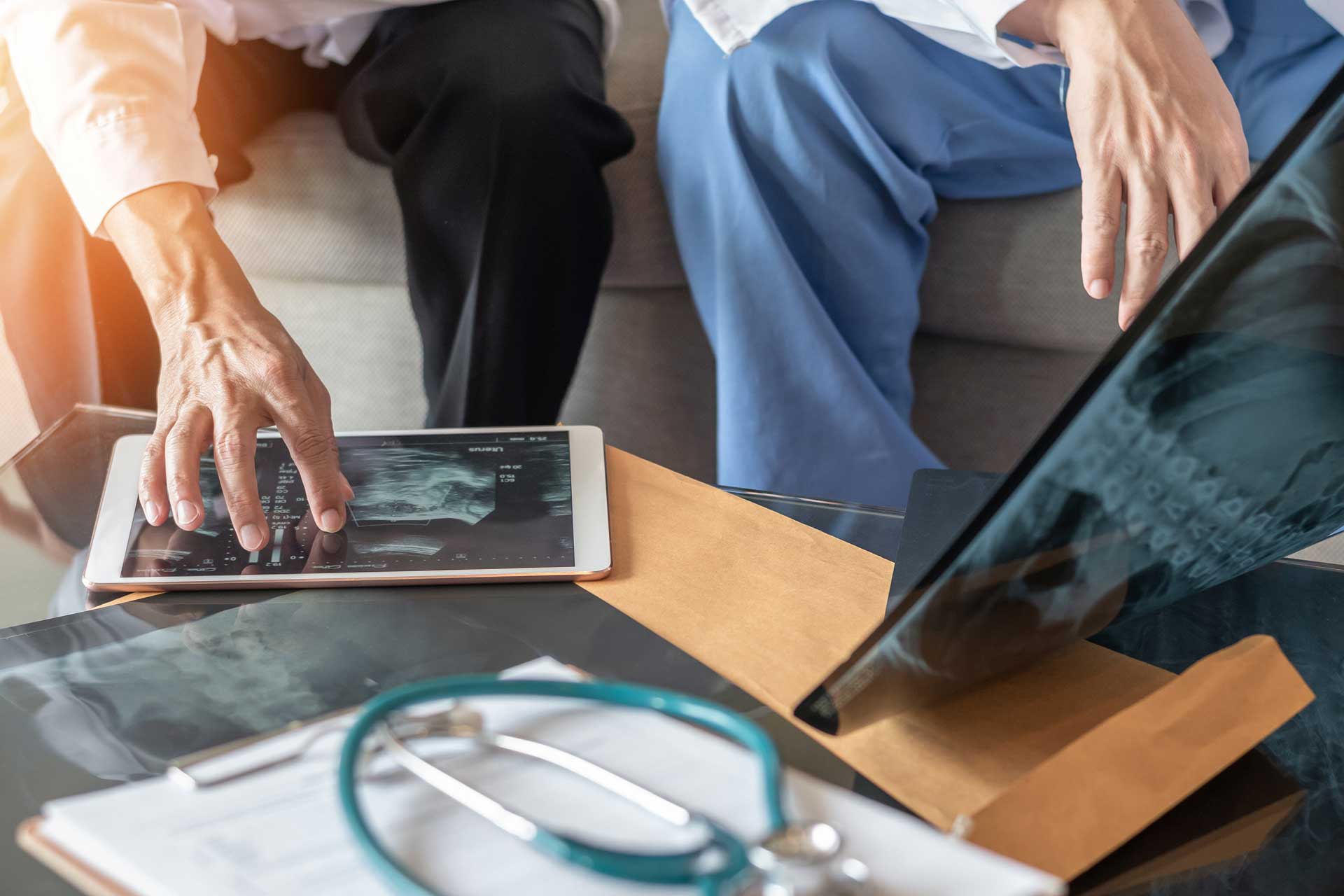 Doctors examining X-rays on a tablet and laptop next to medical documents.