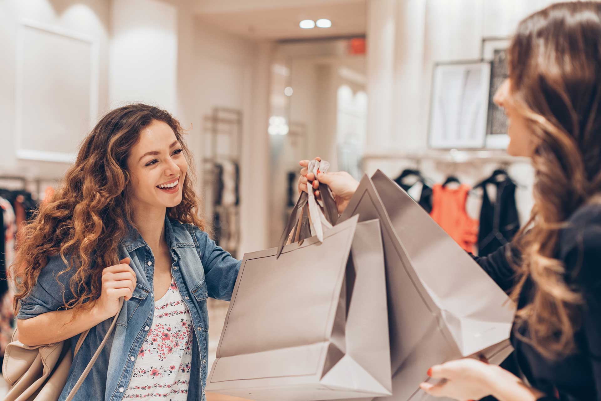 Two women exchanging shopping bags in a clothing store.