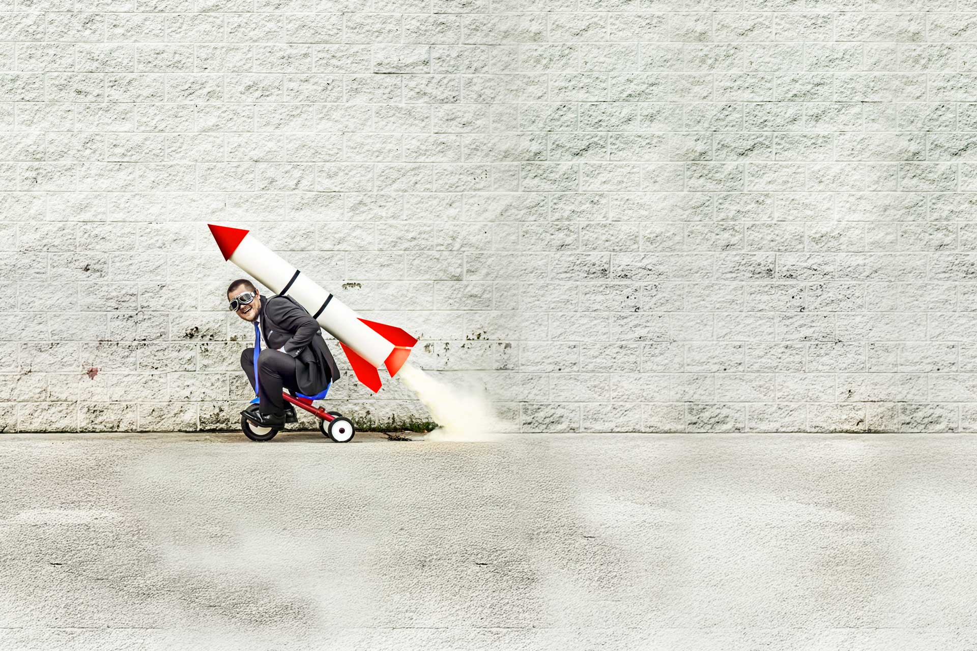 Person on tricycle with digital marketing rocket backpack, against a brick wall.