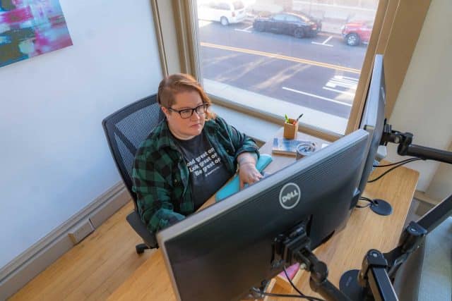 Person creating content at a desk using dual monitors in a bright office space.