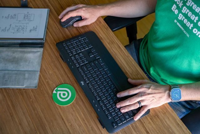 Person managing contract web design at a wooden desk.