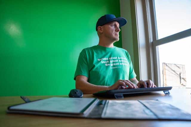Person in green shirt typing SEO tips at a desk, gazing out the window.