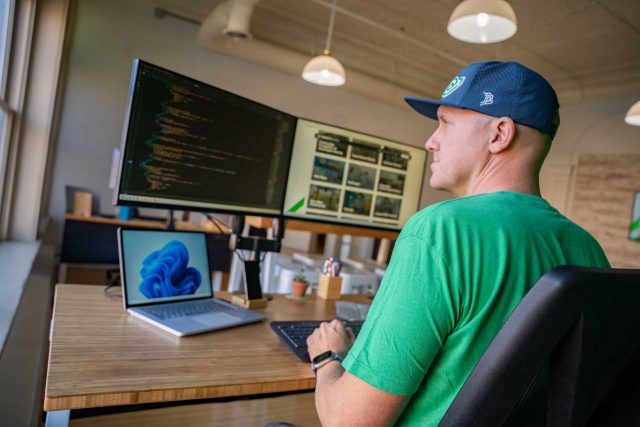Person coding on dual monitors at a desk in an office setting.
