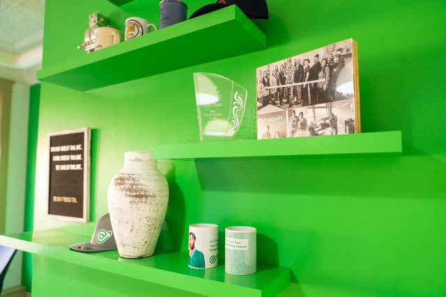 Green shelves with vase, mugs, cap, award, and monochrome photos.
