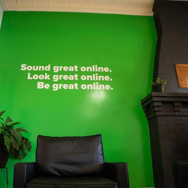 Green wall with motivational text above black chairs near a fireplace.