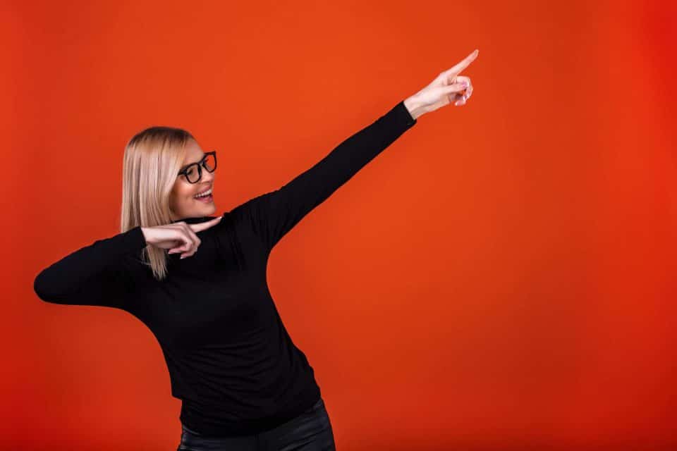Person in black shirt pointing upward against an orange background.