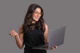 Woman with glasses smiling while looking at a laptop.