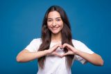 Woman making a heart shape for customer service on Facebook, blue background.