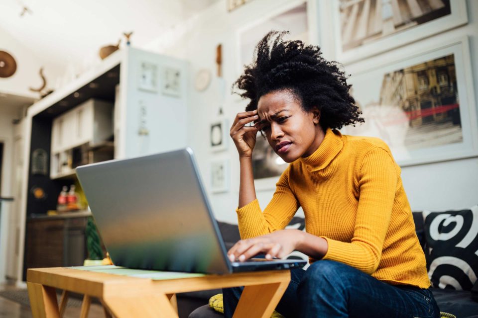 Person in yellow sweater looks puzzled managing online presence on a laptop.