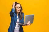 Woman frustrated by website speed while looking at laptop, yellow background.