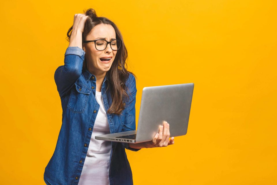 Woman frustrated by website speed while looking at laptop, yellow background.
