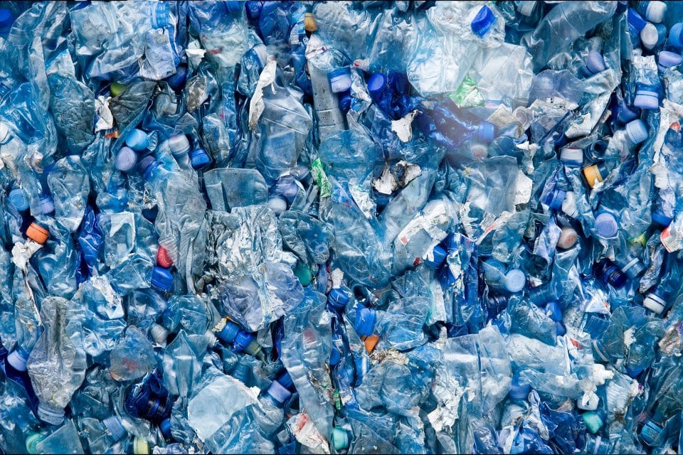 A pile of crushed and discarded blue plastic bottles, densely packed together.