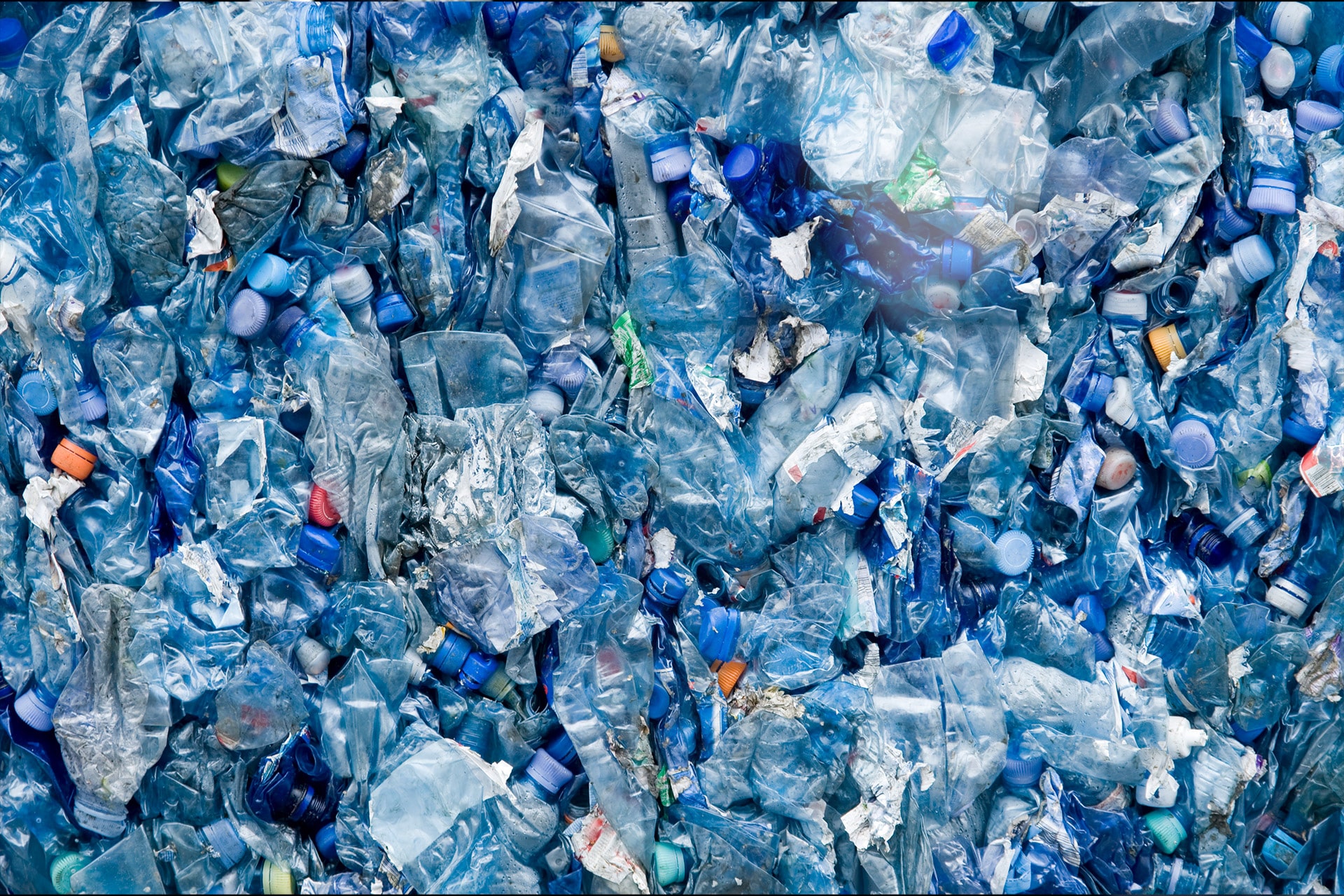 A pile of crushed and discarded blue plastic bottles, densely packed together.