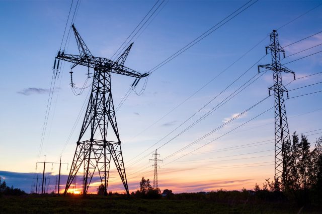 High-voltage power lines and pylons at sunset over a grassy landscape.