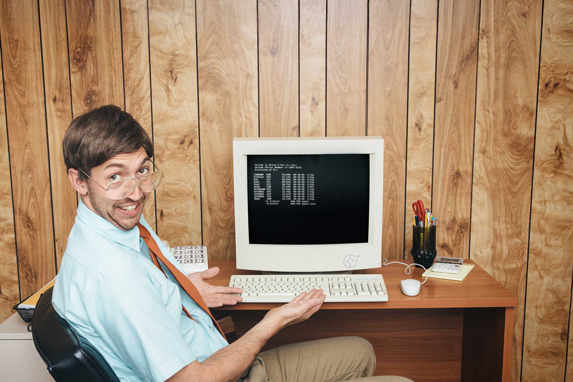 Man with glasses pointing at vintage computer for website hosting.