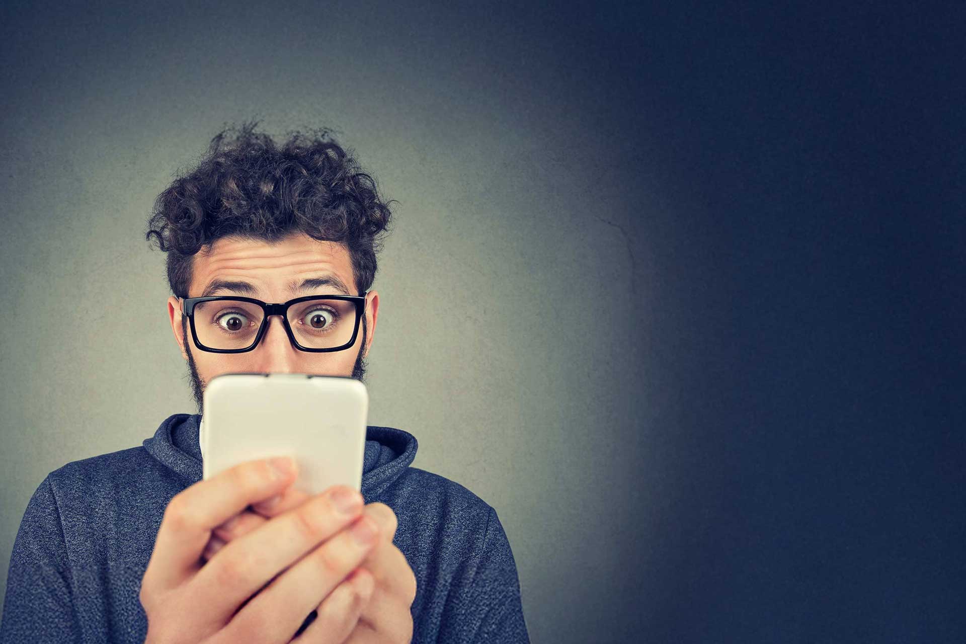 Person with glasses looking surprised at online reviews on a smartphone.