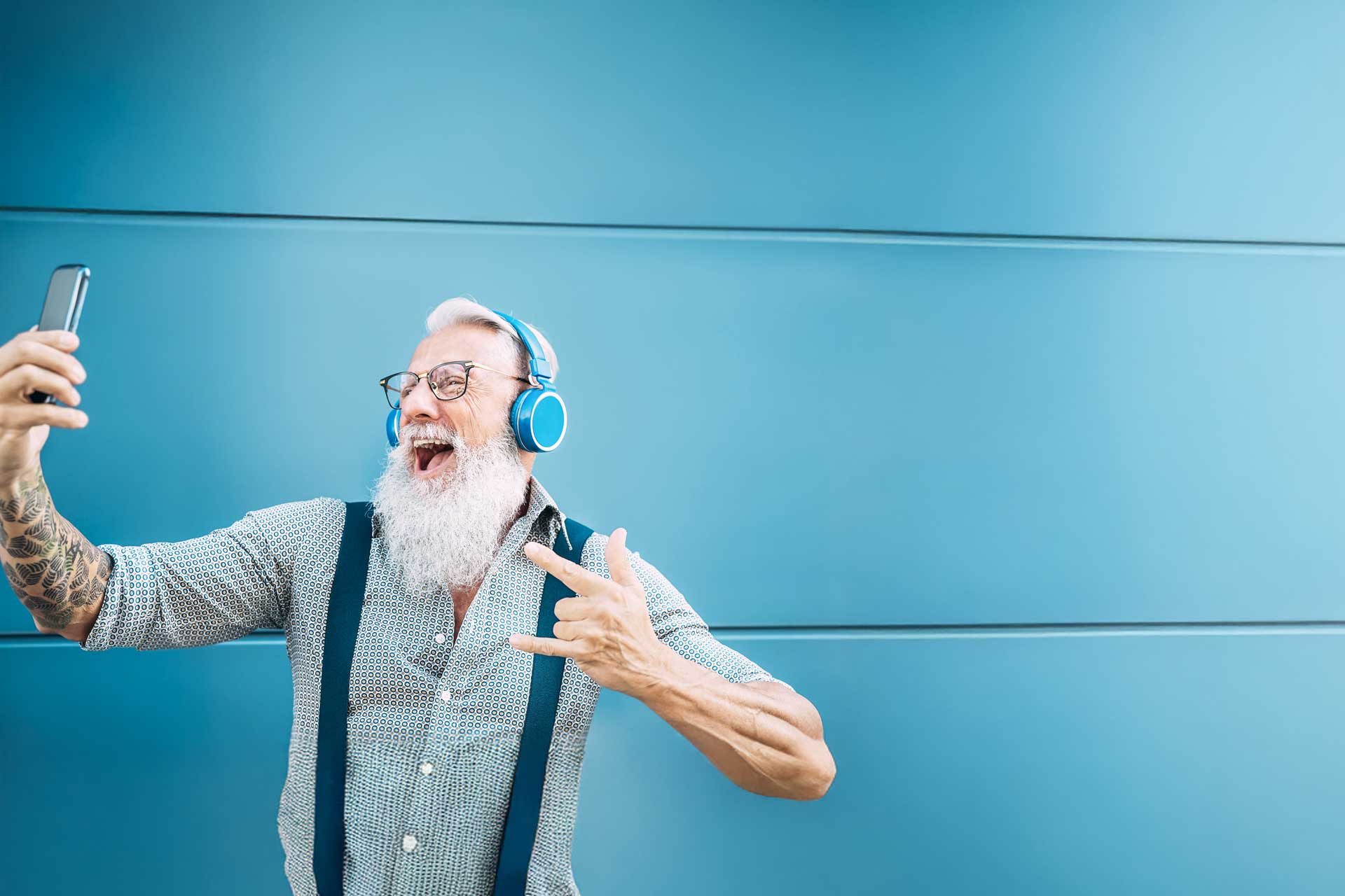 Man wearing headphones, taking a selfie, gesturing energetically for social media.