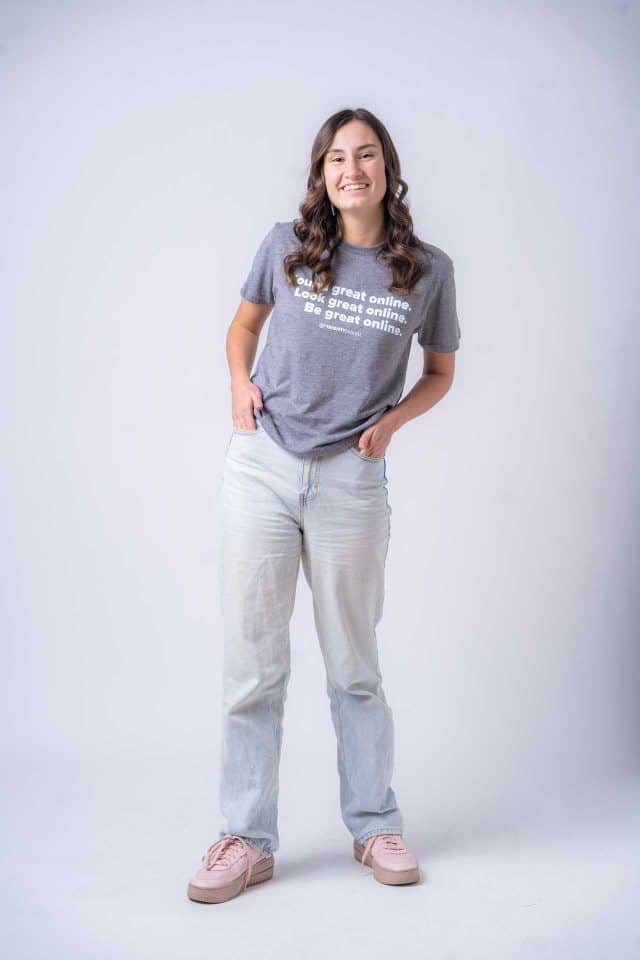 Woman smiling, in gray tee and jeans, standing against an email marketing backdrop.