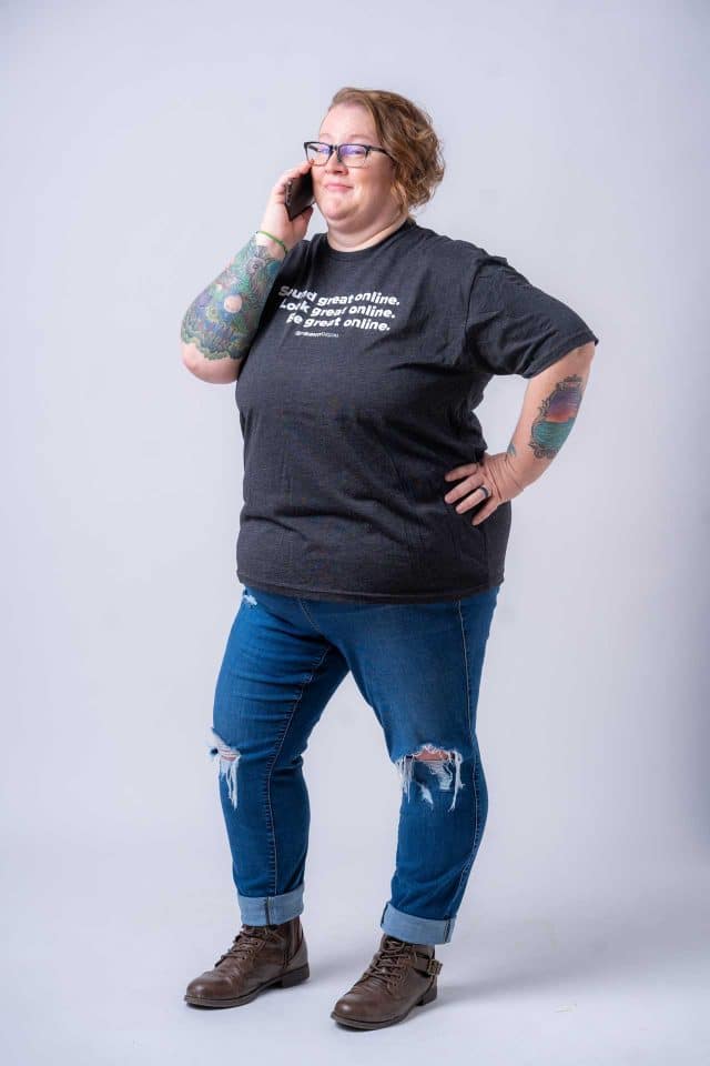 Person with glasses on phone, sporting SEO-themed t-shirt and ripped jeans.