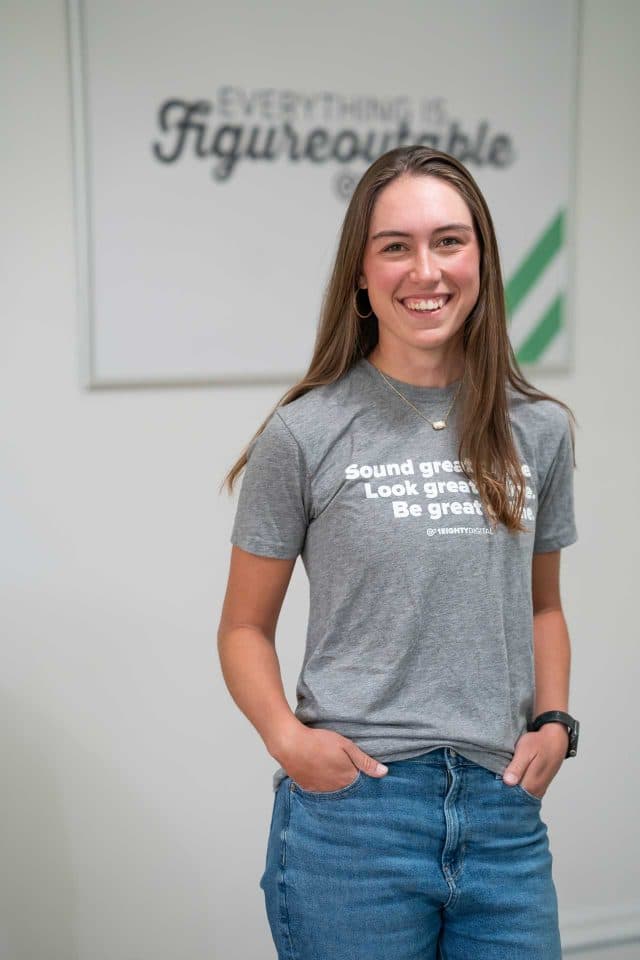 Woman in gray t-shirt and jeans smiles at the camera, showcasing her content creation.