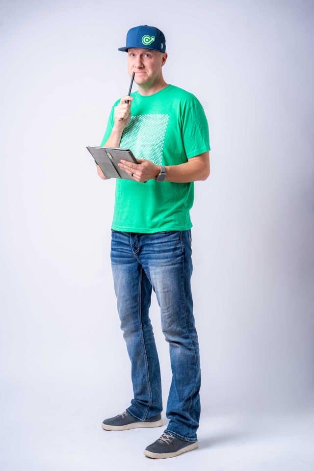 Man in green shirt and cap, holding a pen and tablet, pondering social media.
