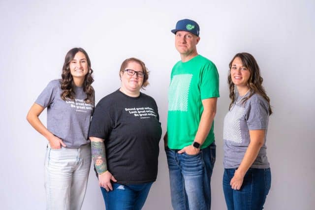Four people standing against a white background, wearing casual t-shirts.