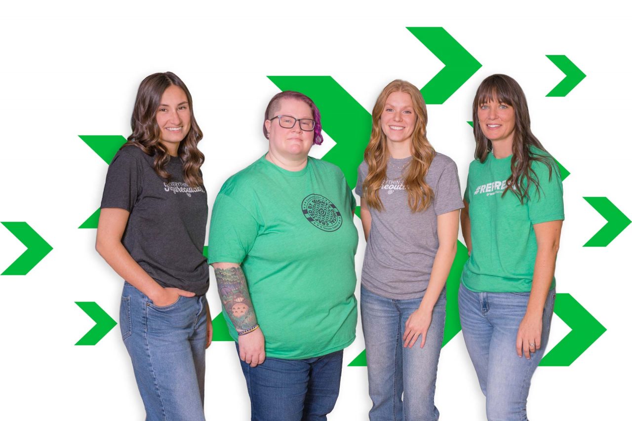 Four people in casual shirts and jeans standing in front of a white background.