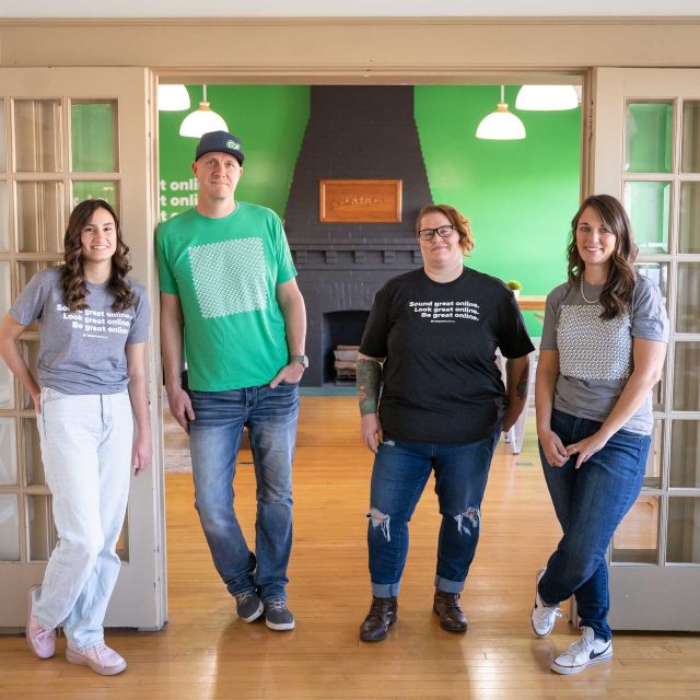 Four people in a cozy, green-walled room, brainstorming content by the fireplace.