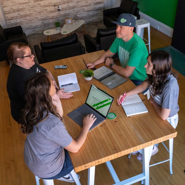 Four people in a meeting, brainstorming web design around a wooden table.