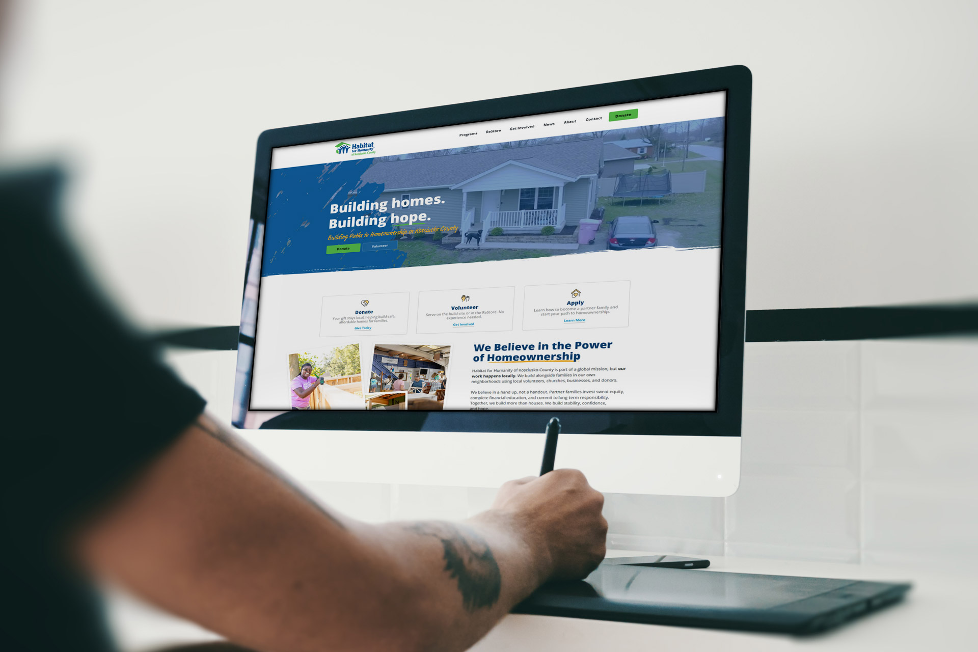 Person using a stylus at a desk with a housing nonprofit website on a monitor.